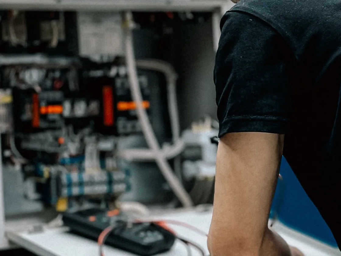 An engineer working at an opened equipment panel, test meter on the bench